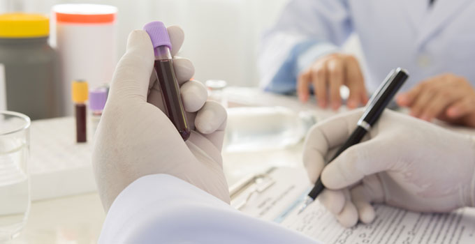 A technician holds a blood sample and writes down information.