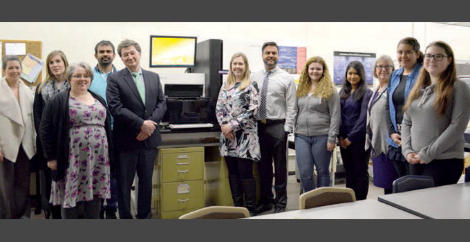 Individuals from OICR and Fleming College pose for a photo in front of the sequencer.