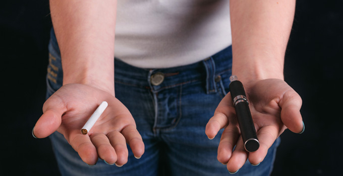 A person holds a cigarette in one hand and an electronic cigarette in the other.