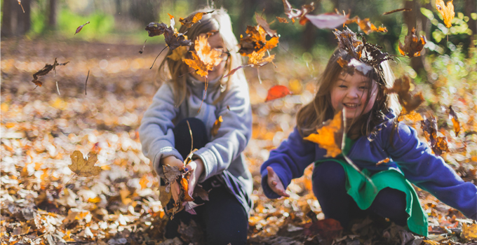 Two young girls play in a pile of autumn leaves.